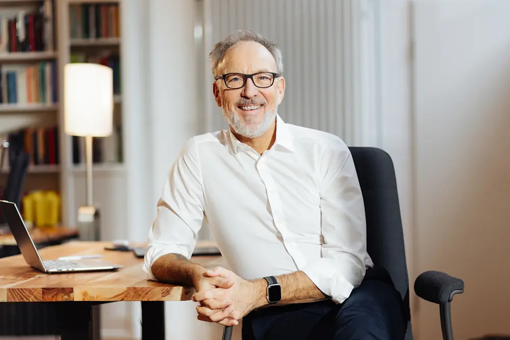 Dr. Armin Straub seitlich aufgelehnt an seinem Schreibtisch mit Blick nach vorne.